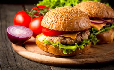 Ev yapımı Hamburger bira ile yakın çekim fotoğraf sığır eti, soğan, domates, marul, peynir ve baharat yaptı. Taze hamburger tatlı patates kızartması ve cips ile ahşap rustik tabloda.