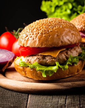 Ev yapımı Hamburger bira ile yakın çekim fotoğraf sığır eti, soğan, domates, marul, peynir ve baharat yaptı. Taze hamburger tatlı patates kızartması ve cips ile ahşap rustik tabloda.