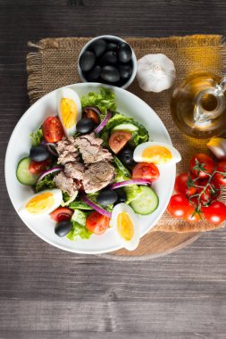 Domates, roka, ton balığı, yumurta, roka, kraker ve baharattan yapılmış taze balık salatası. Tahta arka planda beyaz bir kasede Sezar salatası.