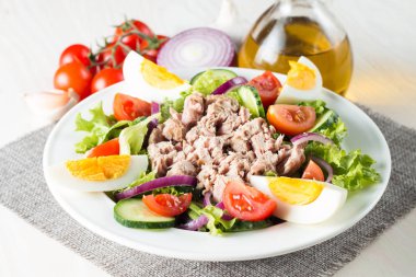 Domates, roka, ton balığı, yumurta, roka, kraker ve baharattan yapılmış taze balık salatası. Tahta arka planda beyaz bir kasede Sezar salatası.