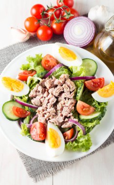 Domates, roka, ton balığı, yumurta, roka, kraker ve baharattan yapılmış taze balık salatası. Tahta arka planda beyaz bir kasede Sezar salatası.