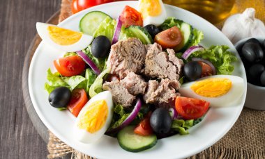 Domates, roka, ton balığı, yumurta, roka, kraker ve baharattan yapılmış taze balık salatası. Tahta arka planda beyaz bir kasede Sezar salatası.