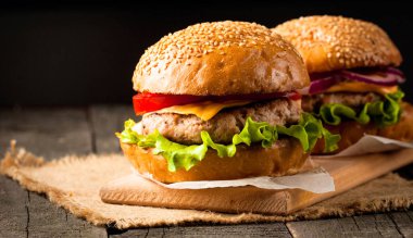 Ev yapımı Hamburger bira ile yakın çekim fotoğraf sığır eti, soğan, domates, marul, peynir ve baharat yaptı. Taze hamburger tatlı patates kızartması ve cips ile ahşap rustik tabloda.