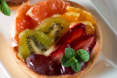 Taze meyve ve meyve ahşap zemin üzerine atmak şekerli tatlı tart. Ahududu, üzüm, çilek, kiraz, kivi, greyfurt ve krema ile lezzetli tatlı pasta.