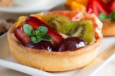 Taze meyve ve meyve ahşap zemin üzerine atmak şekerli tatlı tart. Ahududu, üzüm, çilek, kiraz, kivi, greyfurt ve krema ile lezzetli tatlı pasta.