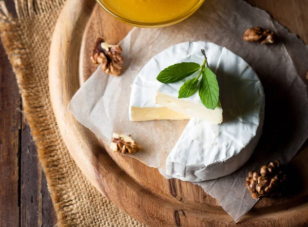 Brie type of cheese. Camembert cheese. Fresh Brie cheese and a slice on a wooden board with nuts, honey and leaves. Italian, French cheese.