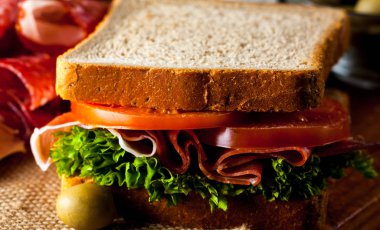 Club sandviç yakın çekim fotoğraf. Eti, jambon, salam, salata, sebze, marul, domates, soğan ve hardal ahşap arka plan üzerinde taze dilimlenmiş siyah ekmek üzerinde sandviç. Zeytin arka plan.