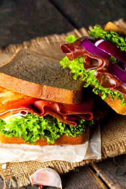 Club sandviç yakın çekim fotoğraf. Eti, jambon, salam, salata, sebze, marul, domates, soğan ve hardal ahşap arka plan üzerinde taze dilimlenmiş siyah ekmek üzerinde sandviç. Zeytin arka plan.