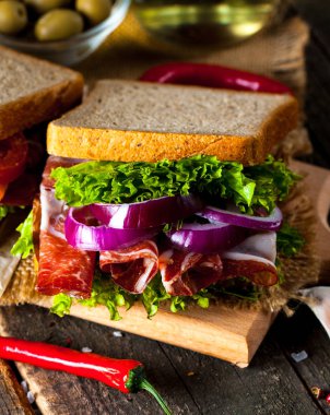 Club sandviç yakın çekim fotoğraf. Eti, jambon, salam, salata, sebze, marul, domates, soğan ve hardal ahşap arka plan üzerinde taze dilimlenmiş siyah ekmek üzerinde sandviç. Zeytin arka plan.