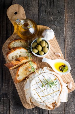 Pişmiş camembert peyniri. Taze Brie peyniri ve bir dilim fındık, tatlım, biberiye ile ahşap bir gemide, baget ekmek ızgara tost ve yaprakları. Peynir Brie türü. İtalyan, Fransız peynir.