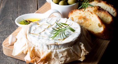 Pişmiş camembert peyniri. Taze Brie peyniri ve bir dilim fındık, tatlım, biberiye ile ahşap bir gemide, baget ekmek ızgara tost ve yaprakları. Peynir Brie türü. İtalyan, Fransız peynir.