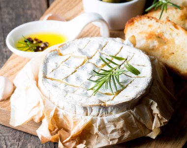 Pişmiş camembert peyniri. Taze Brie peyniri ve bir dilim fındık, tatlım, biberiye ile ahşap bir gemide, baget ekmek ızgara tost ve yaprakları. Peynir Brie türü. İtalyan, Fransız peynir.