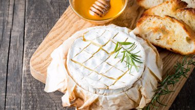 Pişmiş camembert peyniri. Taze Brie peyniri ve bir dilim fındık, tatlım, biberiye ile ahşap bir gemide, baget ekmek ızgara tost ve yaprakları. Peynir Brie türü. İtalyan, Fransız peynir.