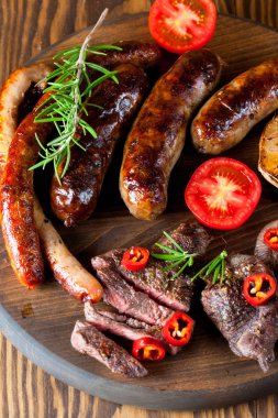 Karışık ızgara et tabağı yakın çekim fotoğraf. Sığır eti, domuz eti, kümes hayvanları, sosis, kızarmış sarımsak, biber biber, ahşap rustik arka plan üzerinde kırmızı domates.