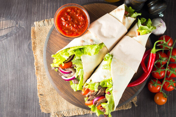 Photo of Mexican sandwich food, burrito, fajita, tacos, wrap made of tortilla, beef, chicken, fresh vegetables on rustic wooden background. Fast food concept. Healthy lunch snack. Copy space. 