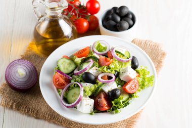 Kiraz domates, ruccola, roka, beyaz peynir, zeytin, salatalık, soğan ve baharat taze Yunan salatası yaptı. Sezar salatası ahşap arka plan üzerinde beyaz bir kase. Sağlıklı organik beslenme gıda kavramı.