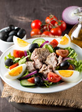 Domates, roka, ton balığı, yumurta, roka, kraker ve baharattan yapılmış taze balık salatası. Tahta arka planda beyaz bir kasede Sezar salatası.