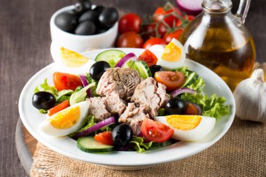 Domates, roka, ton balığı, yumurta, roka, kraker ve baharattan yapılmış taze balık salatası. Tahta arka planda beyaz bir kasede Sezar salatası.