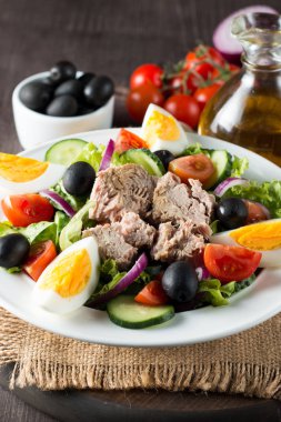 Domates, roka, ton balığı, yumurta, roka, kraker ve baharattan yapılmış taze balık salatası. Tahta arka planda beyaz bir kasede Sezar salatası.