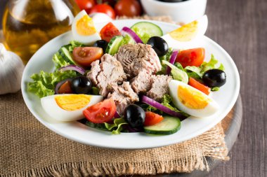 Domates, roka, ton balığı, yumurta, roka, kraker ve baharattan yapılmış taze balık salatası. Tahta arka planda beyaz bir kasede Sezar salatası.