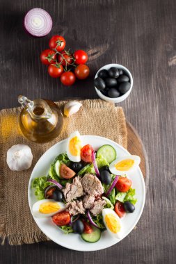 Domates, roka, ton balığı, yumurta, roka, kraker ve baharattan yapılmış taze balık salatası. Tahta arka planda beyaz bir kasede Sezar salatası.