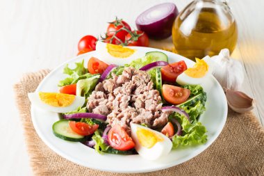 Domates, roka, ton balığı, yumurta, roka, kraker ve baharattan yapılmış taze balık salatası. Tahta arka planda beyaz bir kasede Sezar salatası.