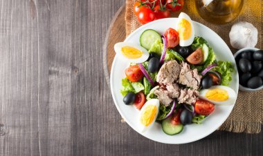 Domates, roka, ton balığı, yumurta, roka, kraker ve baharattan yapılmış taze balık salatası. Tahta arka planda beyaz bir kasede Sezar salatası.