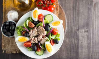 Domates, roka, ton balığı, yumurta, roka, kraker ve baharattan yapılmış taze balık salatası. Tahta arka planda beyaz bir kasede Sezar salatası.