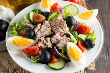 Domates, roka, ton balığı, yumurta, roka, kraker ve baharattan yapılmış taze balık salatası. Tahta arka planda beyaz bir kasede Sezar salatası.