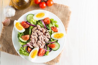 Domates, roka, ton balığı, yumurta, roka, kraker ve baharattan yapılmış taze balık salatası. Tahta arka planda beyaz bir kasede Sezar salatası.