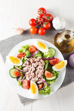 Domates, roka, ton balığı, yumurta, roka, kraker ve baharattan yapılmış taze balık salatası. Tahta arka planda beyaz bir kasede Sezar salatası.