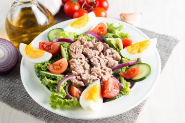 Domates, roka, ton balığı, yumurta, roka, kraker ve baharattan yapılmış taze balık salatası. Tahta arka planda beyaz bir kasede Sezar salatası.