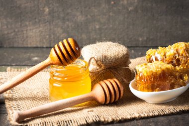 Tatlım gelen ahşap bal ayı gri rustik ahşap arka plan üzerinde bir kavanoza damlama