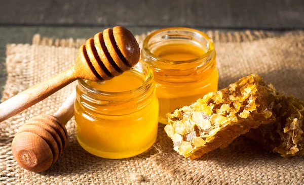 Tatlım gelen ahşap bal ayı gri rustik ahşap arka plan üzerinde bir kavanoza damlama