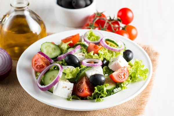 Fresh Greek salad made of cherry tomato, ruccola, arugula, feta, olives, cucumbers, onion and spices. Caesar salad in a white bowl on wooden background. Healthy organic diet food concept.