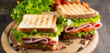 Club sandviç yakın çekim fotoğraf. Eti, jambon, salam, salata, sebze, marul, domates, soğan ve hardal ahşap arka plan üzerinde taze dilimlenmiş siyah ekmek üzerinde sandviç. Zeytin arka plan.