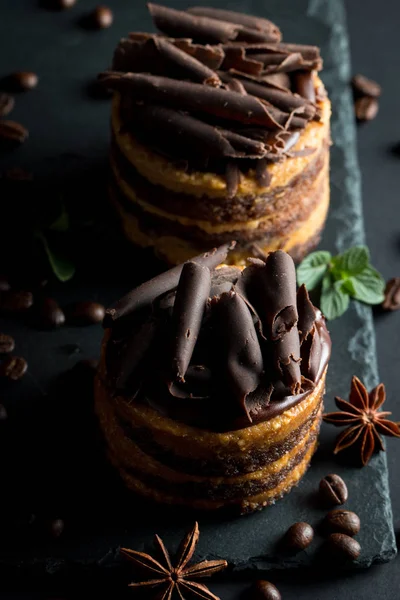 Chocolate cakes on black slatter board with mint, coffee beans on dark background, closeup photo. Fresh, tasty dessert food concept.