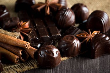 Koyu, beyaz ve sütlü çikolata yığını, cips çeşitleri. Kaba ahşap arka planda çikolata ve kahve çekirdekleri. Baharatlar, tarçın. Seçici makro odaklanma. Çikolata arkaplanı. Tatlılar