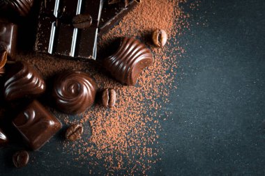 Koyu, beyaz ve sütlü çikolata yığını, cips çeşitleri. Kaba ahşap arka planda çikolata ve kahve çekirdekleri. Baharatlar, tarçın. Seçici makro odaklanma. Çikolata arkaplanı. Tatlılar