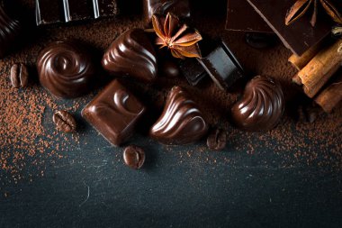 Koyu, beyaz ve sütlü çikolata yığını, cips çeşitleri. Kaba ahşap arka planda çikolata ve kahve çekirdekleri. Baharatlar, tarçın. Seçici makro odaklanma. Çikolata arkaplanı. Tatlılar