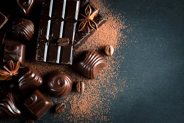 Koyu, beyaz ve sütlü çikolata yığını, cips çeşitleri. Kaba ahşap arka planda çikolata ve kahve çekirdekleri. Baharatlar, tarçın. Seçici makro odaklanma. Çikolata arkaplanı. Tatlılar
