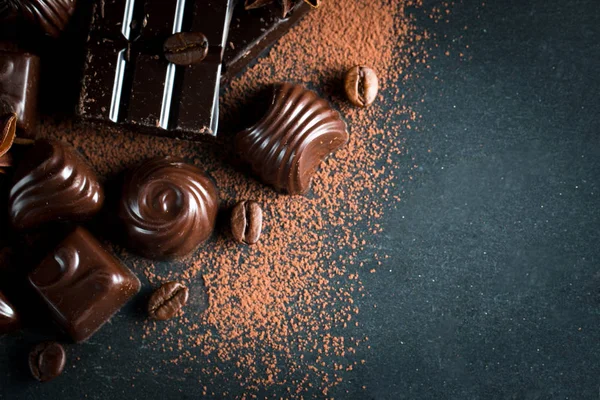 Koyu, beyaz ve sütlü çikolata yığını, cips çeşitleri. Kaba ahşap arka planda çikolata ve kahve çekirdekleri. Baharatlar, tarçın. Seçici makro odaklanma. Çikolata arkaplanı. Tatlılar