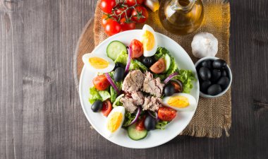 Domates, roka, ton balığı, yumurta, roka, kraker ve baharattan yapılmış taze balık salatası. Tahta arka planda beyaz bir kasede Sezar salatası.