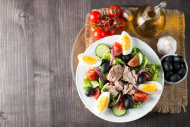 Domates, roka, ton balığı, yumurta, roka, kraker ve baharattan yapılmış taze balık salatası. Tahta arka planda beyaz bir kasede Sezar salatası.