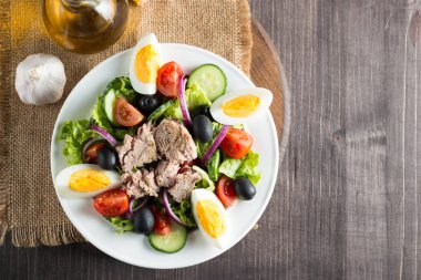 Domates, roka, ton balığı, yumurta, roka, kraker ve baharattan yapılmış taze balık salatası. Tahta arka planda beyaz bir kasede Sezar salatası.