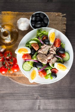 Domates, roka, ton balığı, yumurta, roka, kraker ve baharattan yapılmış taze balık salatası. Tahta arka planda beyaz bir kasede Sezar salatası.