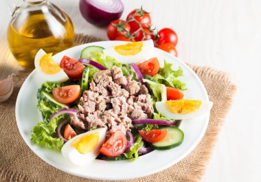 Domates, roka, ton balığı, yumurta, roka, kraker ve baharattan yapılmış taze balık salatası. Tahta arka planda beyaz bir kasede Sezar salatası.