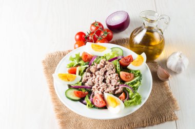 Domates, roka, ton balığı, yumurta, roka, kraker ve baharattan yapılmış taze balık salatası. Tahta arka planda beyaz bir kasede Sezar salatası.