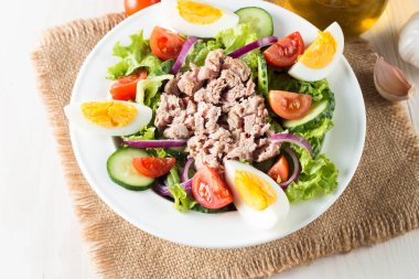 Domates, roka, ton balığı, yumurta, roka, kraker ve baharattan yapılmış taze balık salatası. Tahta arka planda beyaz bir kasede Sezar salatası.