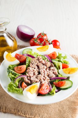 Domates, roka, ton balığı, yumurta, roka, kraker ve baharattan yapılmış taze balık salatası. Tahta arka planda beyaz bir kasede Sezar salatası.